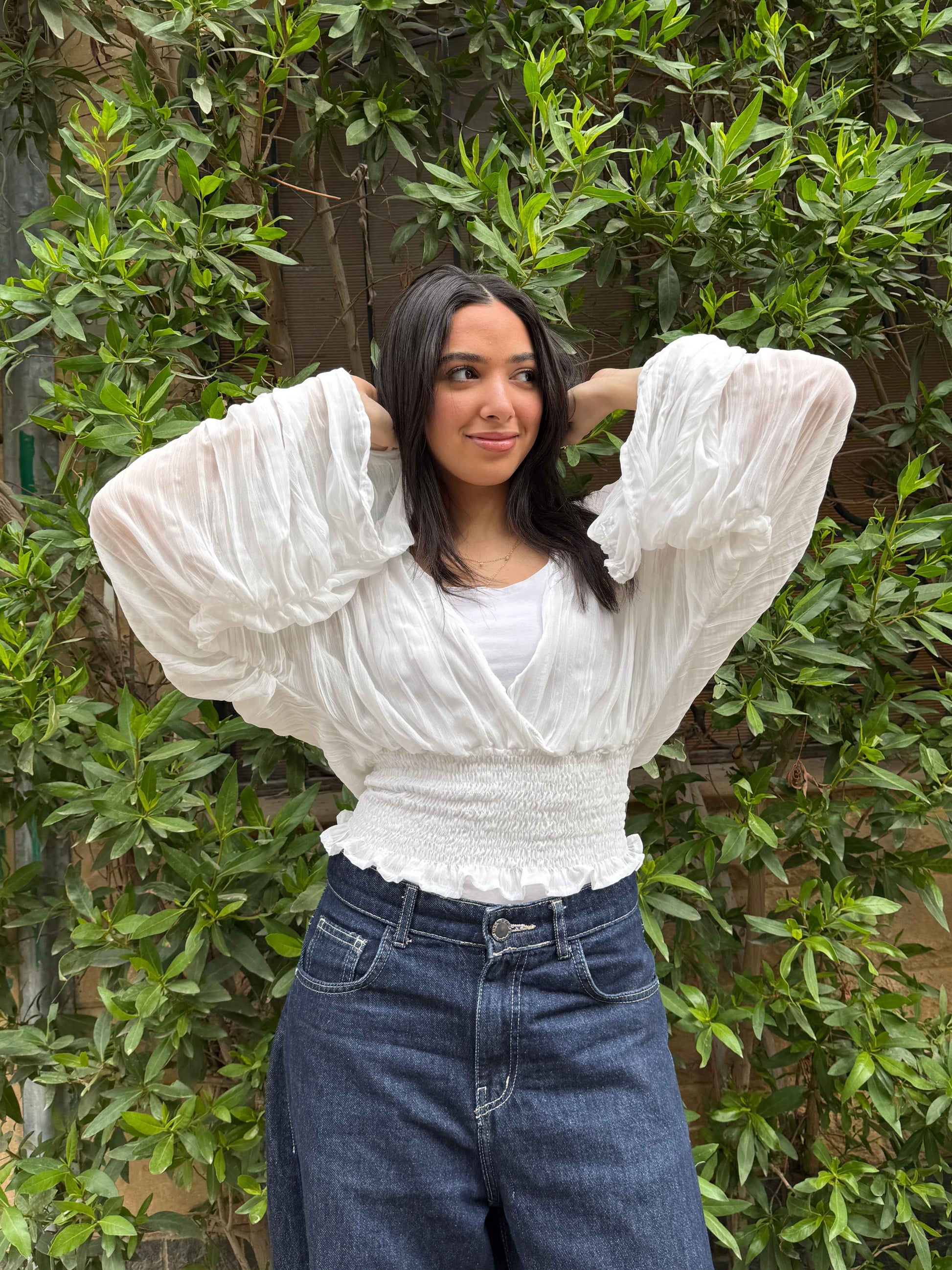 Ocean Breeze Blouse – chic white textured blouse with oversized pleated sleeves and a smocked waist, styled with dark denim for an effortless feminine look.